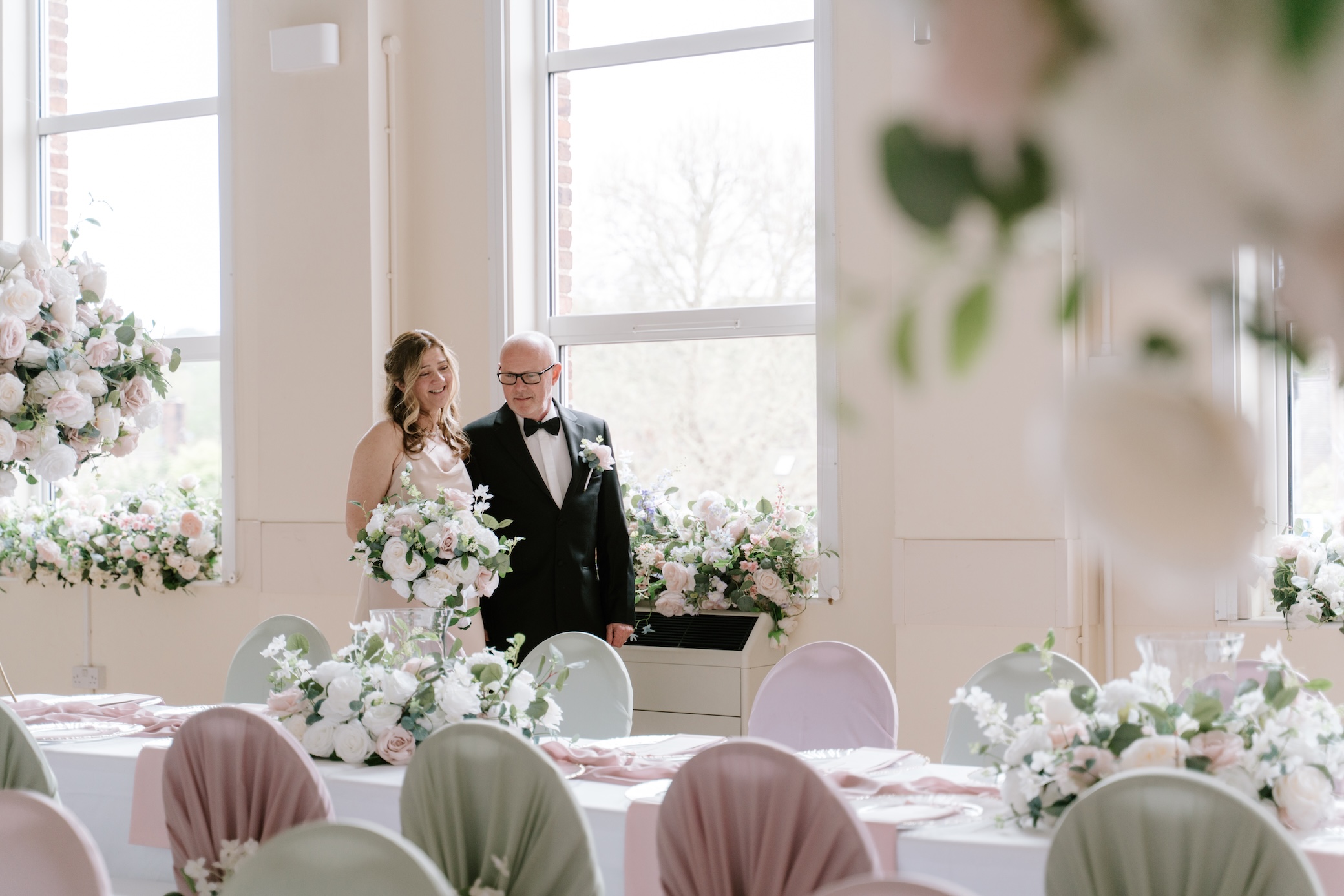 A bride and groom standing in the bright main hall among floral arrangements