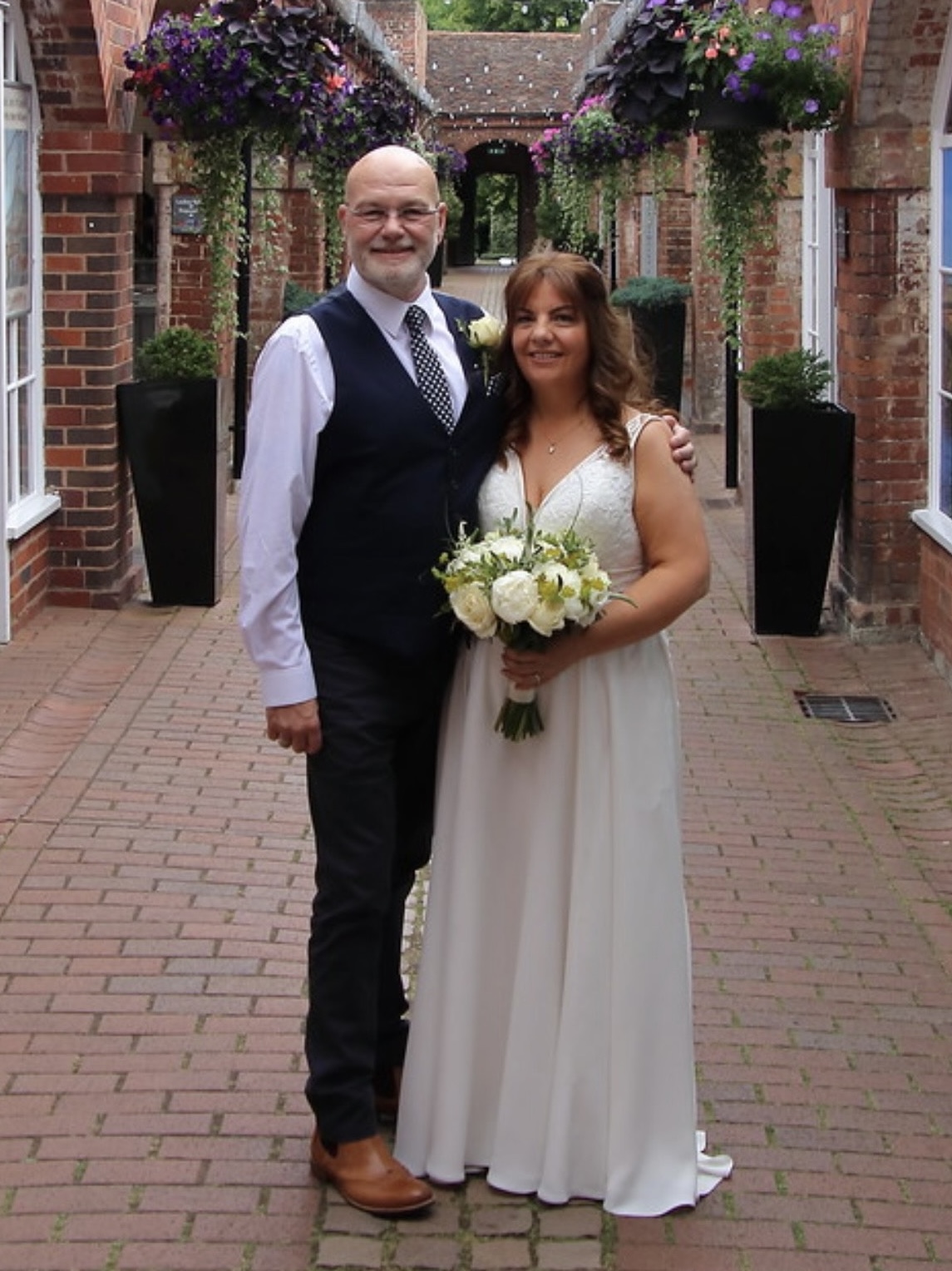 A bride and groom in the historic Shambles courtyard at Bewdley Museum, surrounded by brick buildings and hanging flower baskets